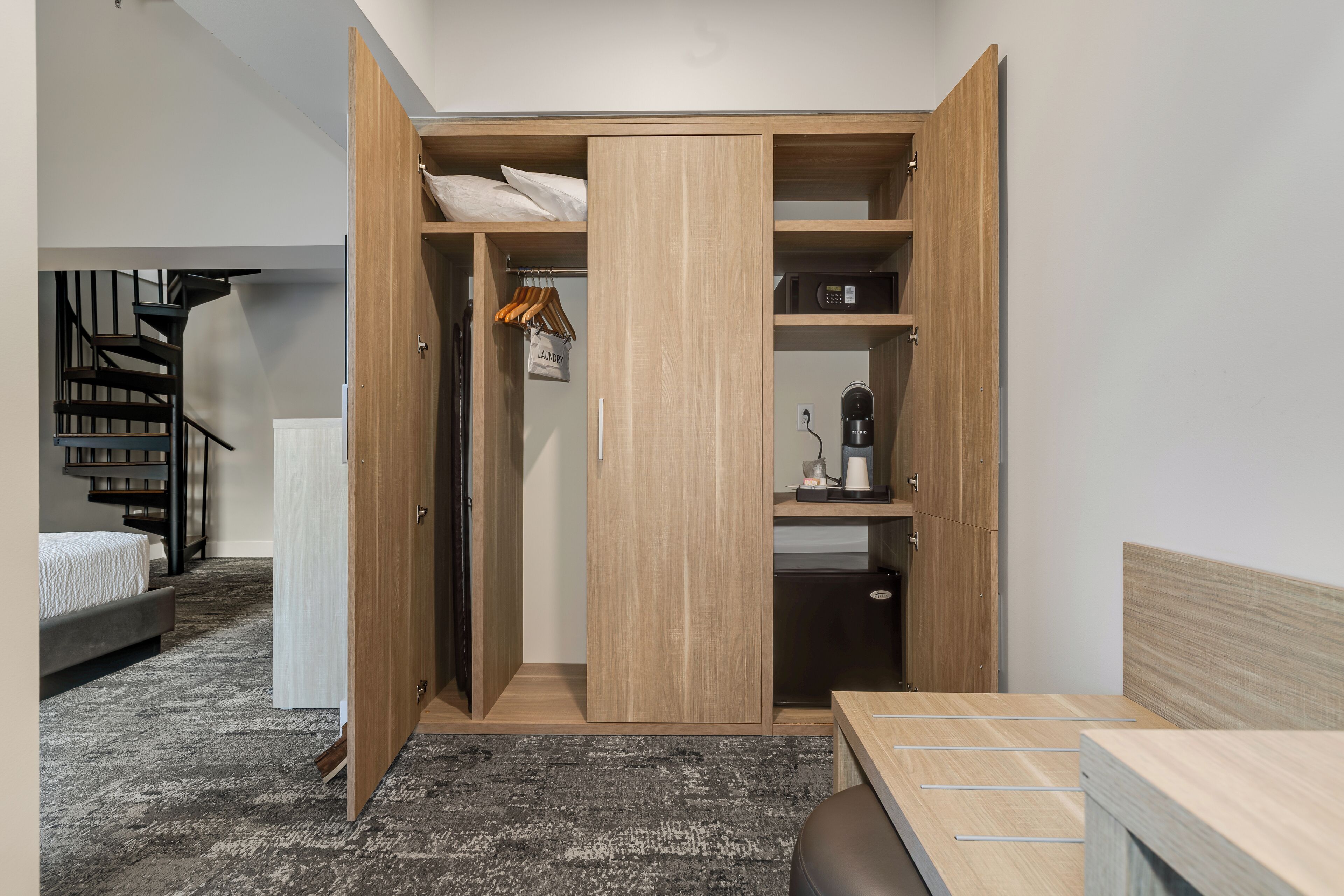 A bedroom with a bed, a wooden wardrobe, a desk, and a staircase.