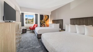 Habitación de hotel con dos camas, televisión, una silla roja y un ventanal con vistas al exterior.