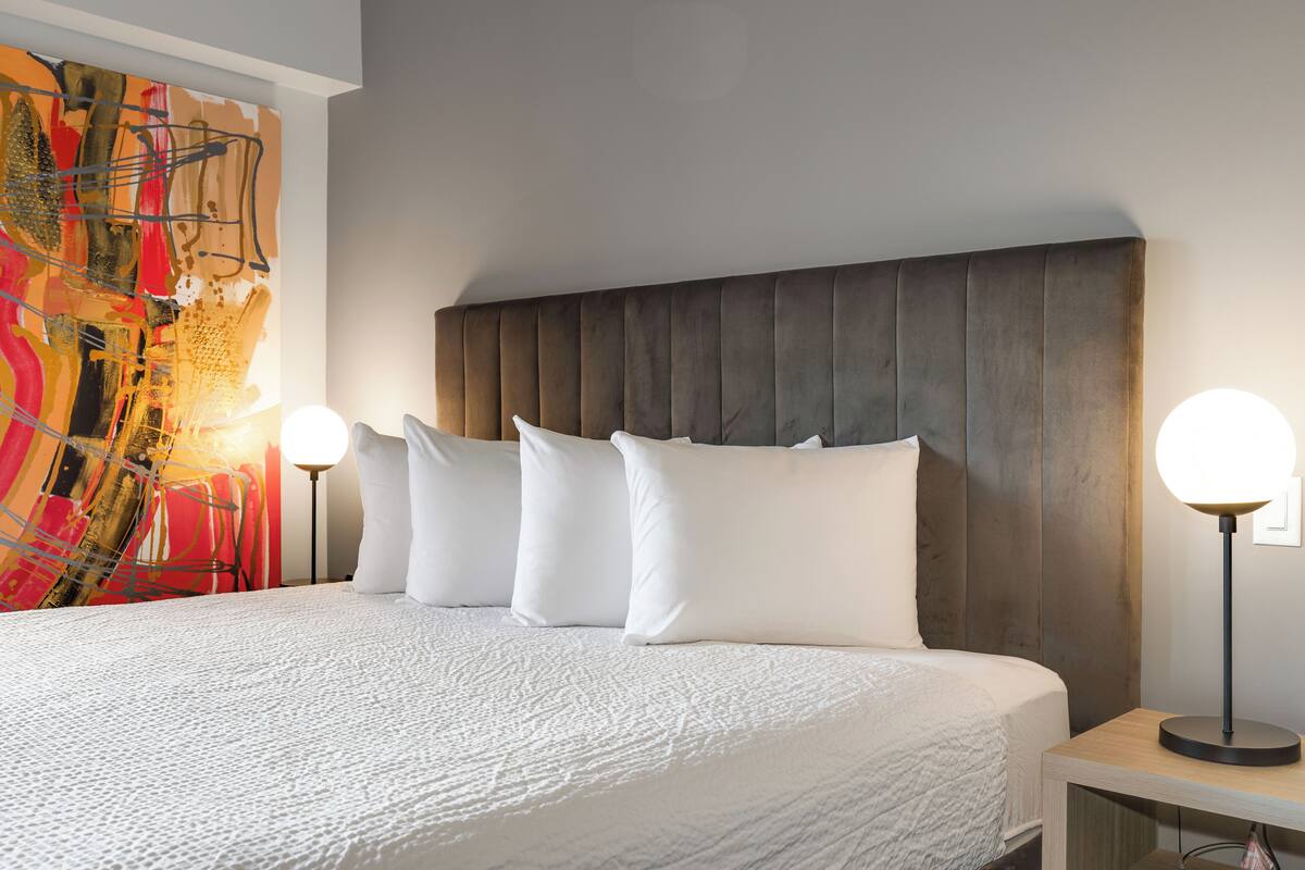 A neatly made bed with white linens, a wooden headboard, and two bedside lamps.