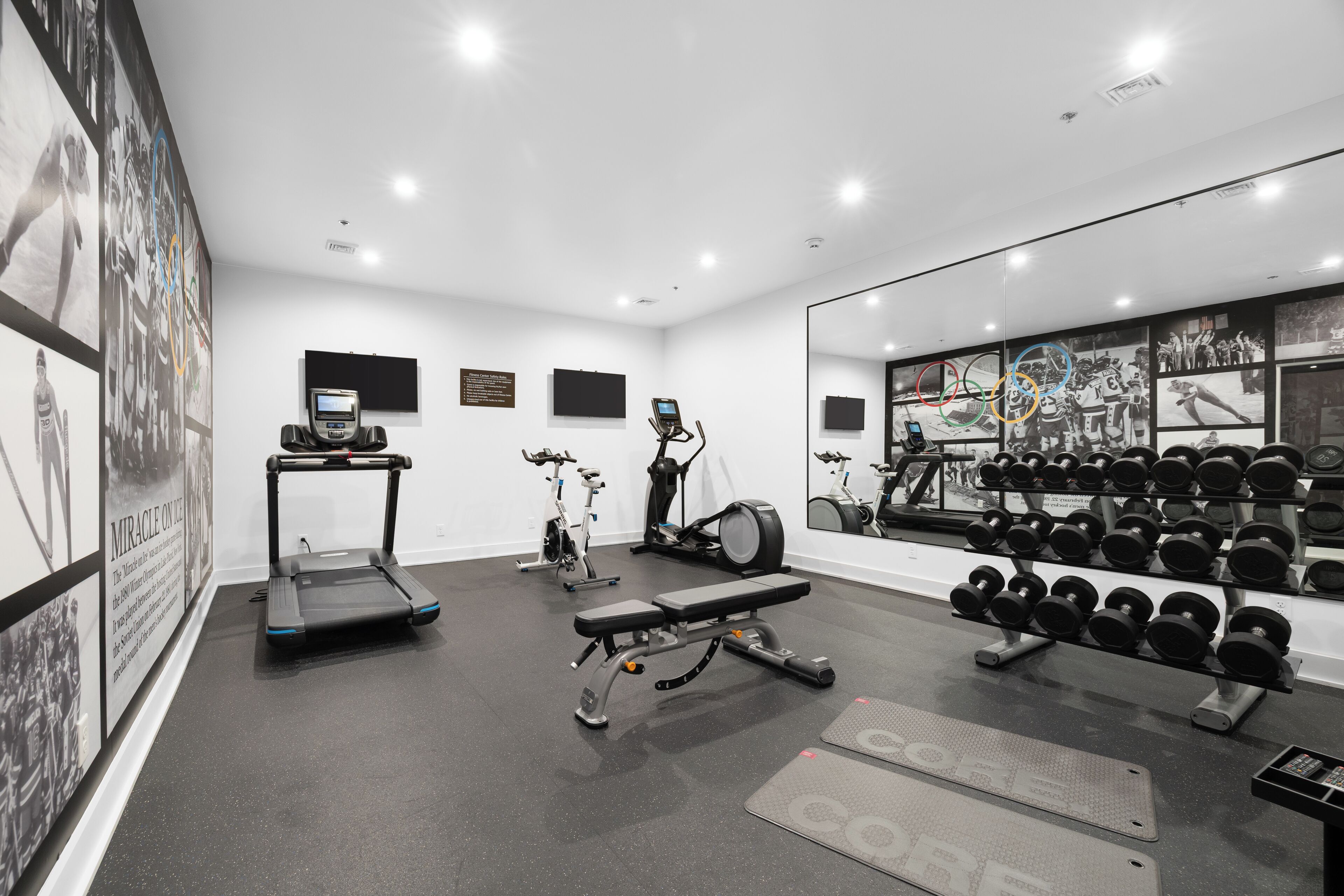A modern gym with treadmills, an elliptical, a bench press, and a rack of dumbbells.