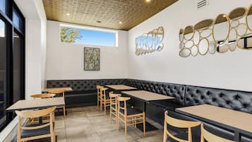 A modern restaurant with a black leather booth seating, wooden tables, and chairs.
