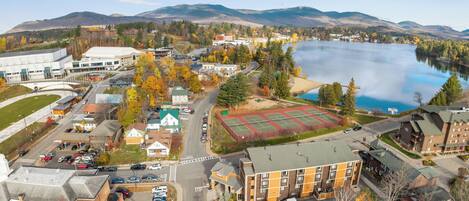 Un hotel de varios pisos con estacionamiento, cancha de tenis y vistas a un lago y montañas.