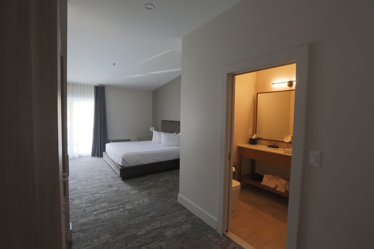 A hotel room with a bed, a bathroom with a mirror, and a door leading to another room.