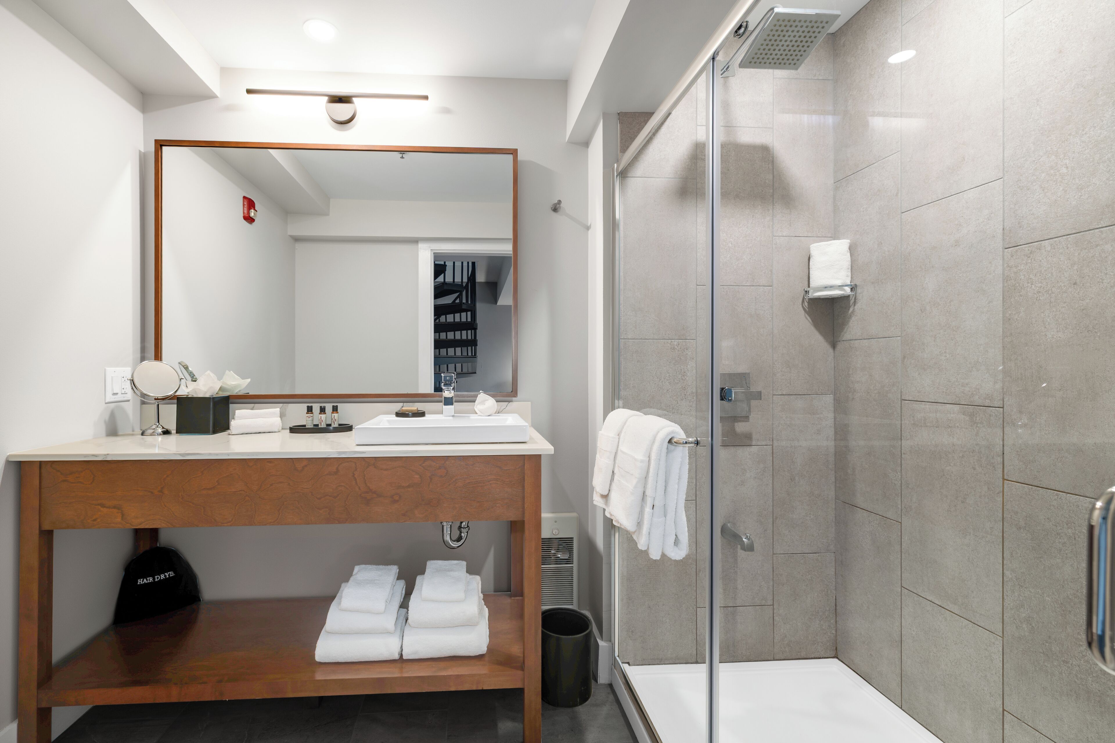 A modern bathroom with a wooden vanity, a large mirror, a glass shower enclosure, and neatly folded towels.
