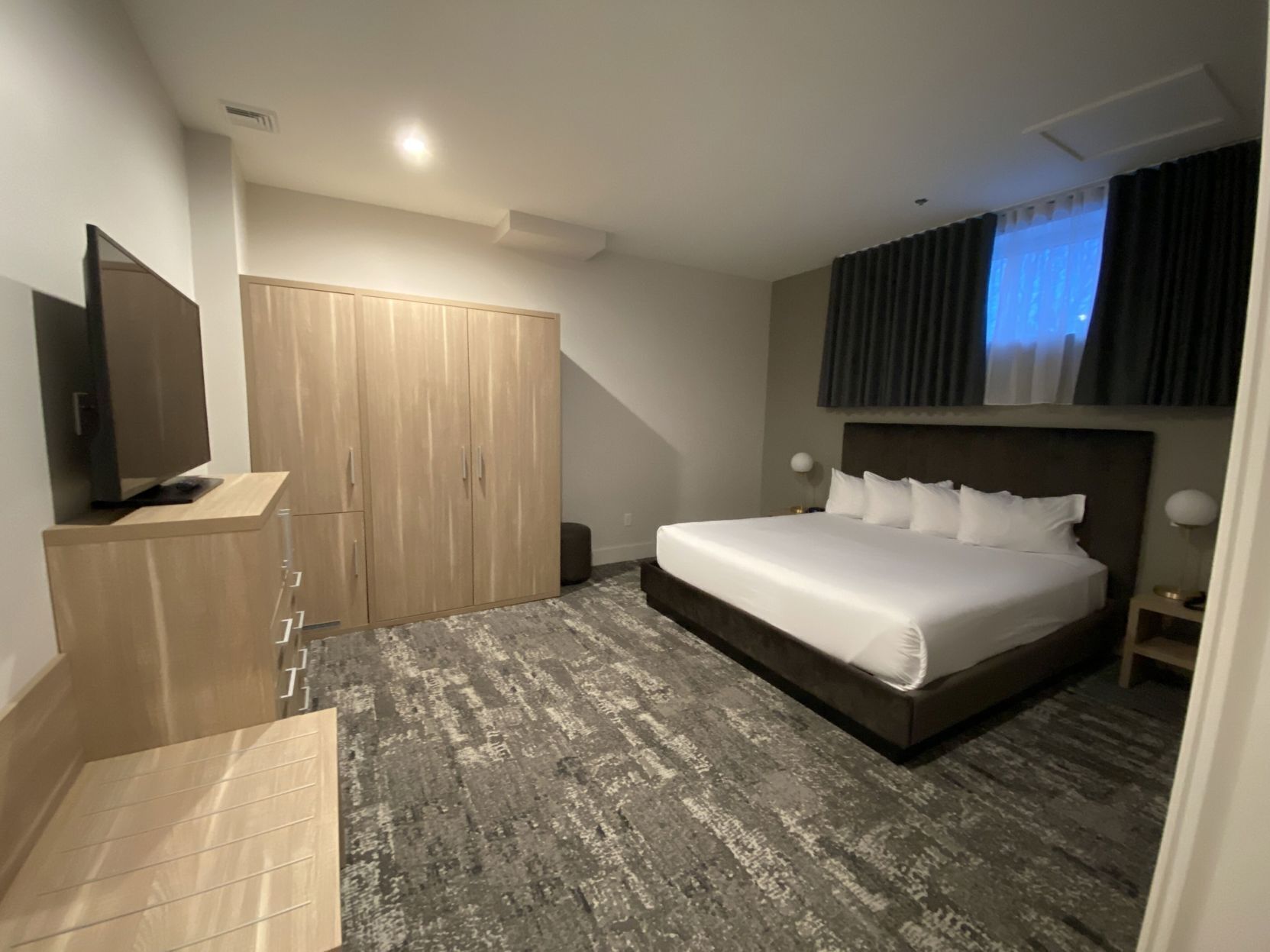 A hotel room with a bed, a TV, a wardrobe, and a small table.