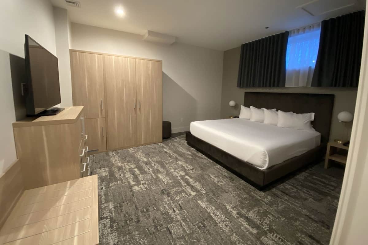 A hotel room with a bed, a TV, a wardrobe, and a small table.