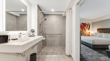 A modern bathroom with a shower, toilet, and sink, and a bedroom with a bed and a painting.