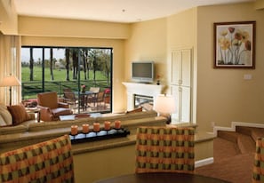 A living room with a sofa, chairs, a fireplace, a television, and a large window with a view of a golf course.