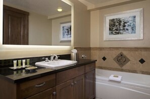 Une salle de bain avec un grand miroir, un lavabo, une baignoire et une œuvre d’art encadrée accrochée au mur.