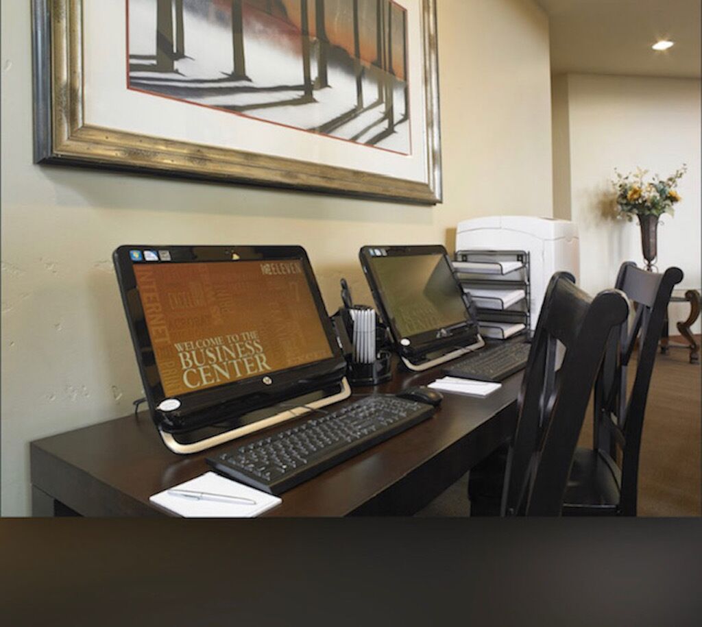 A reception desk with two laptops displaying a welcome screen, a framed abstract painting, and a vase with flowers in the background.
