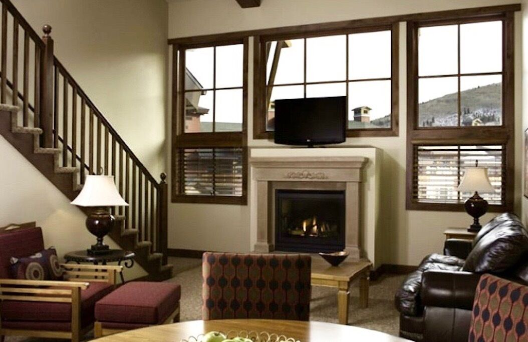 Una sala de estar acogedora con una chimenea, un televisor montado encima y una escalera que sube a un nivel superior.