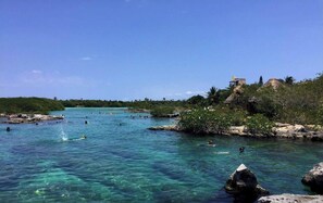 Une zone côtière caractérisée par une eau turquoise et limpide, des affleurements rocheux et quelques bâtiments situés sur la plage.