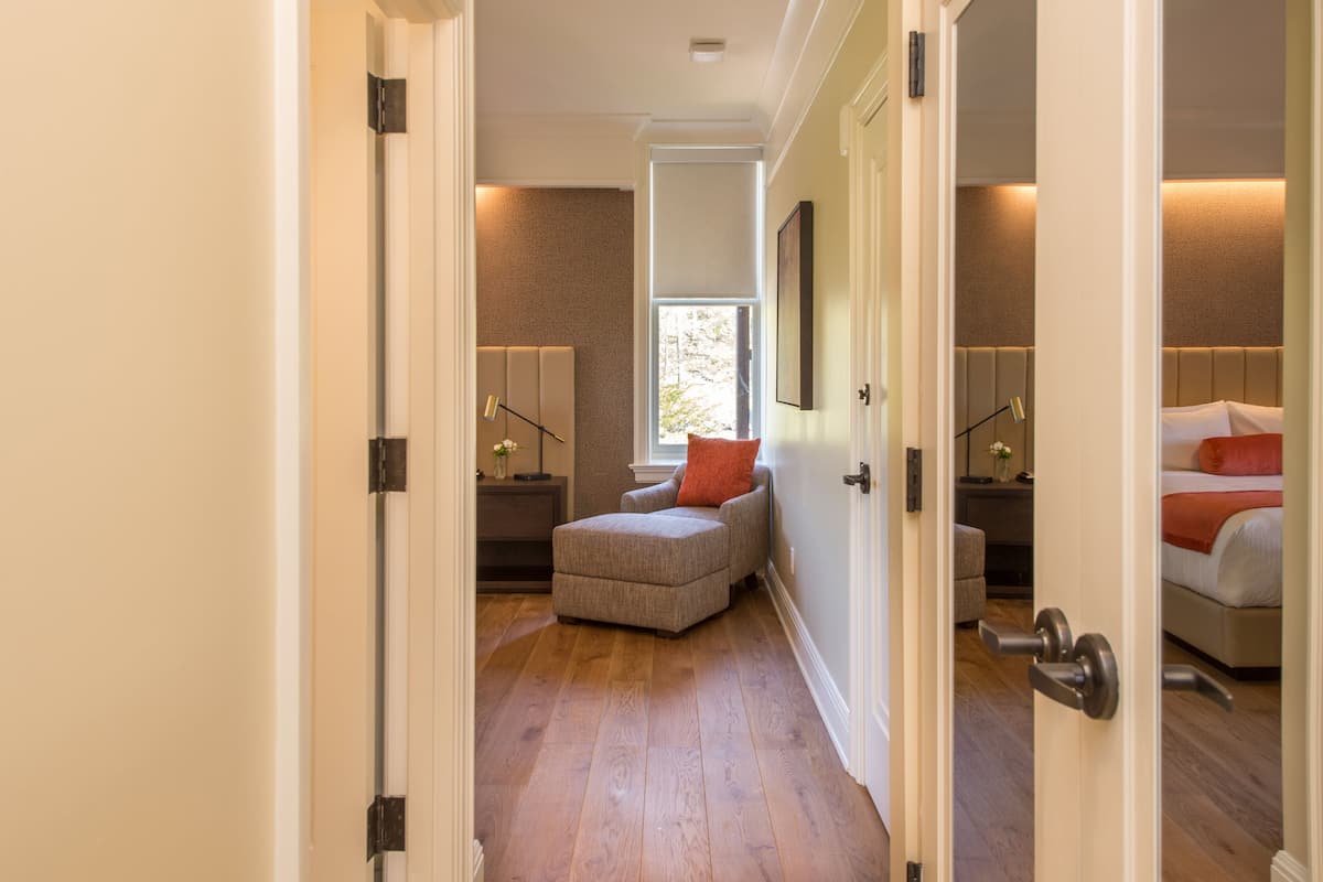 A hallway leading to a bedroom with a bed, a nightstand, and a chair.