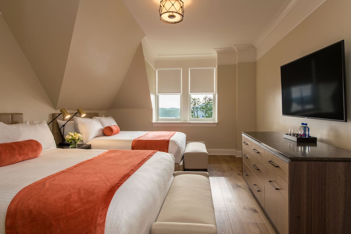 A bedroom with two beds, a dresser, a TV, and a window with a view.
