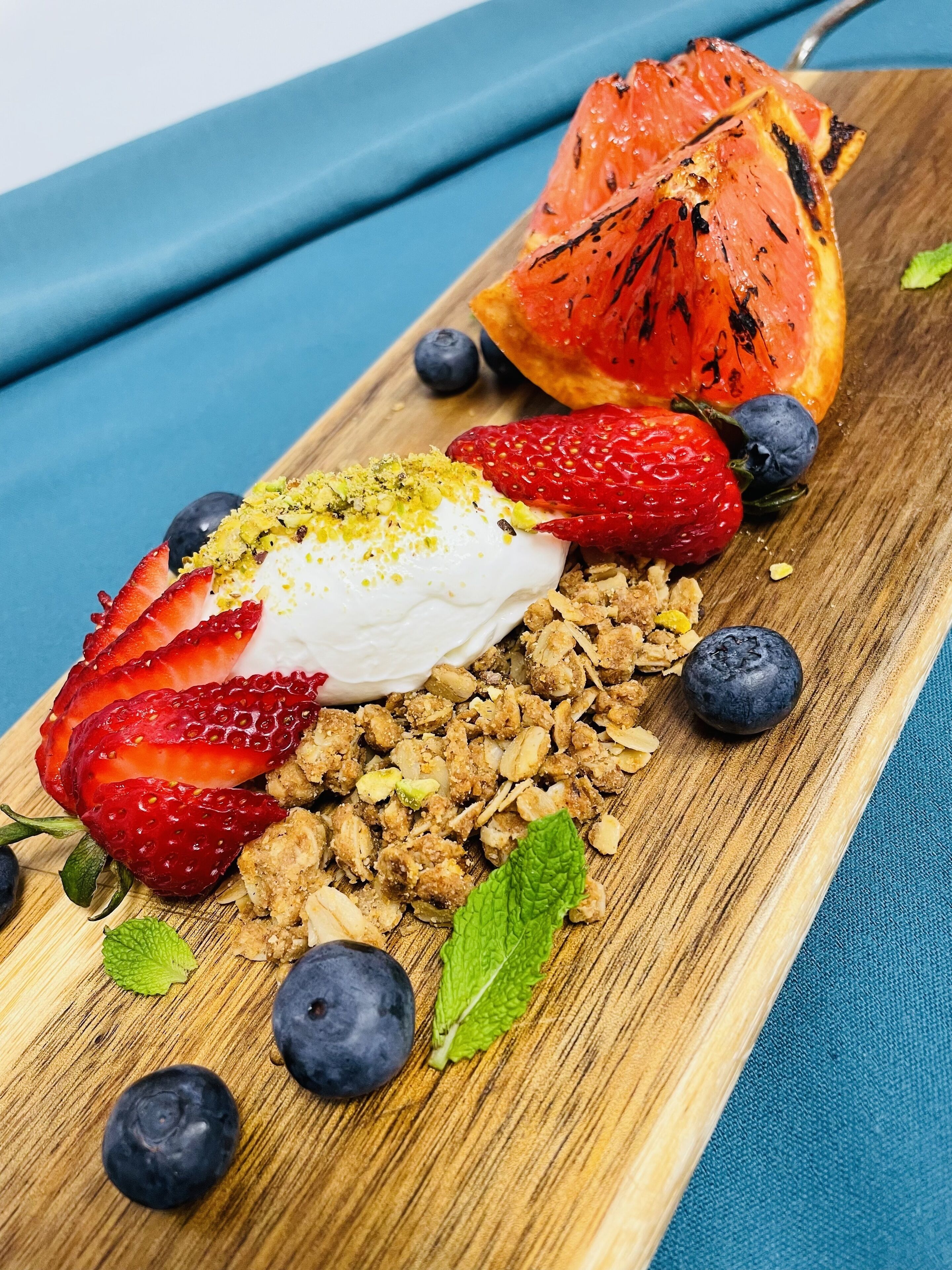 Sobremesa com morangos, amoras e uma fruta grelhada sobre uma tábua de madeira.