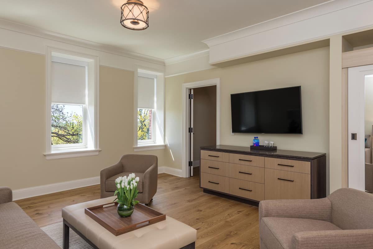 A living room with a flat-screen TV, a beige sofa, a coffee table with a tray and flowers, and a wooden cabinet.