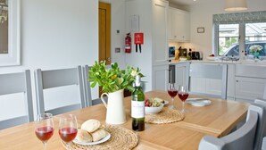 A modern kitchen with white cabinets, a wooden dining table, and a view of the outside through a window. - 4 bedroom accommodation in Trelights, near Port Isaac (Trelights, near Port Isaac)