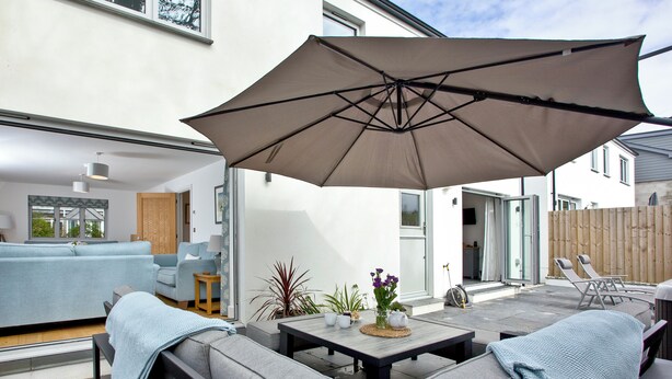 A modern outdoor living area with a sofa, a table with a vase of flowers, and a large umbrella. - 4 bedroom accommodation in Trelights, near Port Isaac (Trelights, near Port Isaac)