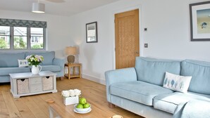 A living room with a sofa, a coffee table, a lamp, and a door. - 4 bedroom accommodation in Trelights, near Port Isaac (Trelights, near Port Isaac)