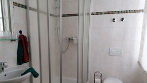 Baño con ducha envuelta en vidrio, lavabo, inodoro y perchero para toallas.