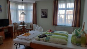 A hotel room with a bed, a desk, a chair, a television, and a window with curtains. - Pension Schöne (Grossrohrsdorf)