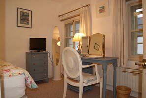 A bedroom with a bed, a dresser, a chair, a desk with a lamp, a mirror, and a window with curtains.