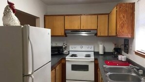 Une cuisine de taille réduite, avec des meubles de rangement en bois, un réfrigérateur blanc, une cuisinière et un évier.