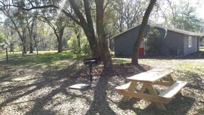Une table de pique-nique et une boîte aux lettres se trouvent dans une zone boisée, avec un petit bâtiment en arrière-plan.