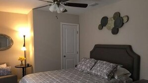 Une chambre à coucher comprenant un lit, un ventilateur de plafond, une table de chevet, une lampe et un élément de décoration murale.