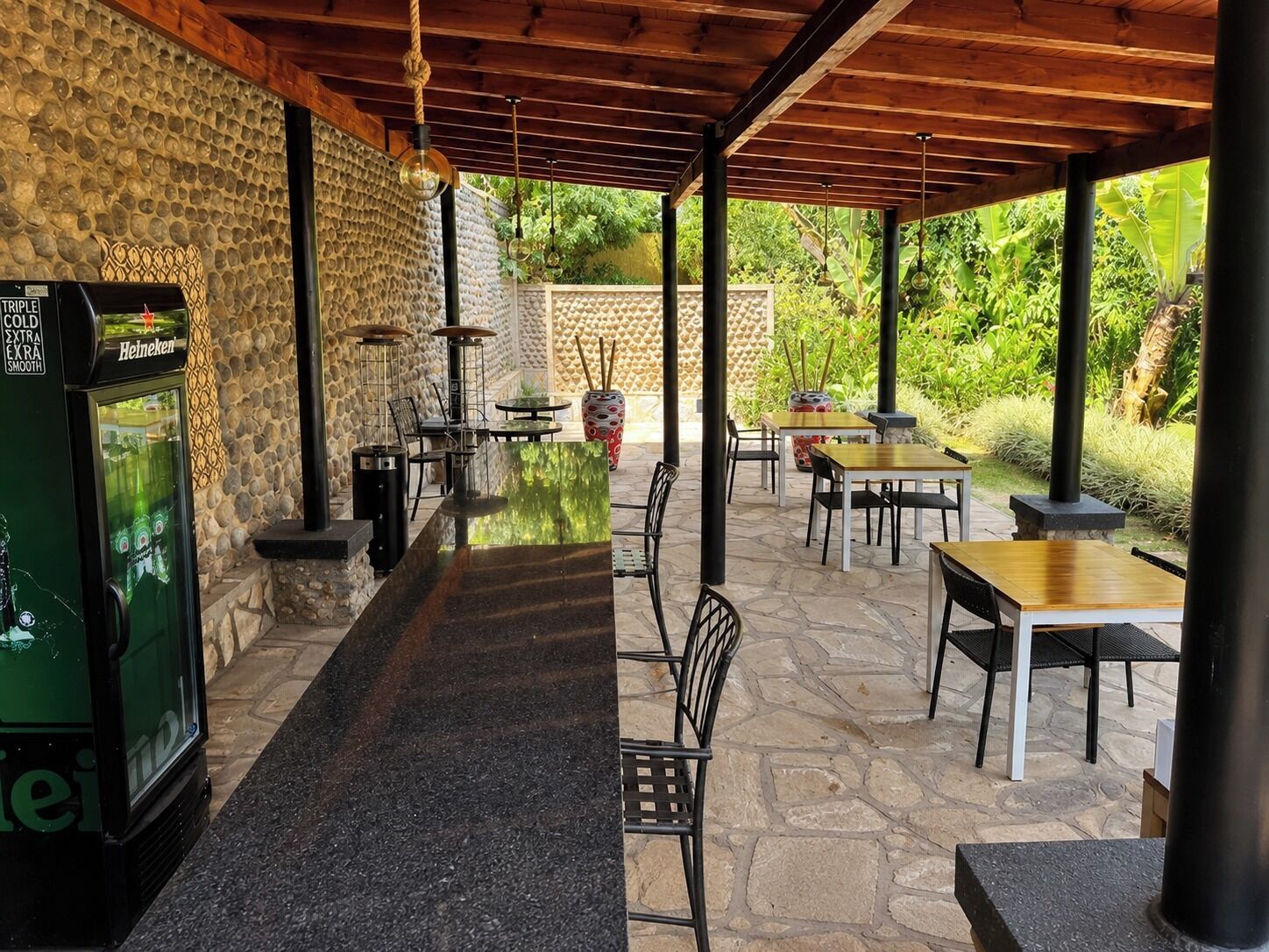 An outdoor bar area with stone walls, tables, chairs, and a Heineken refrigerator.