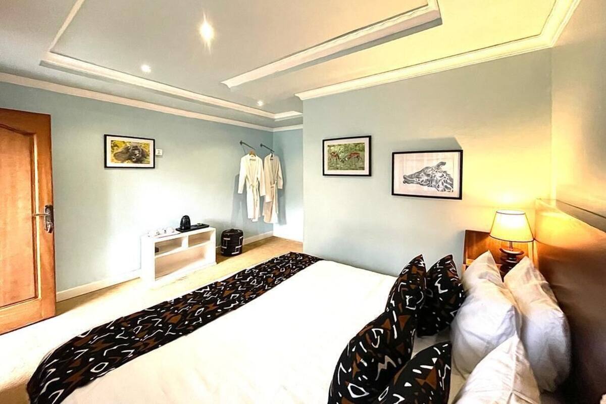 Habitación de hotel con cama, mesita de noche con lámpara, armario y perchero.