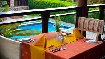 A dining table set with yellow napkins, silverware, and a menu board, overlooking a swimming pool and lush greenery.
