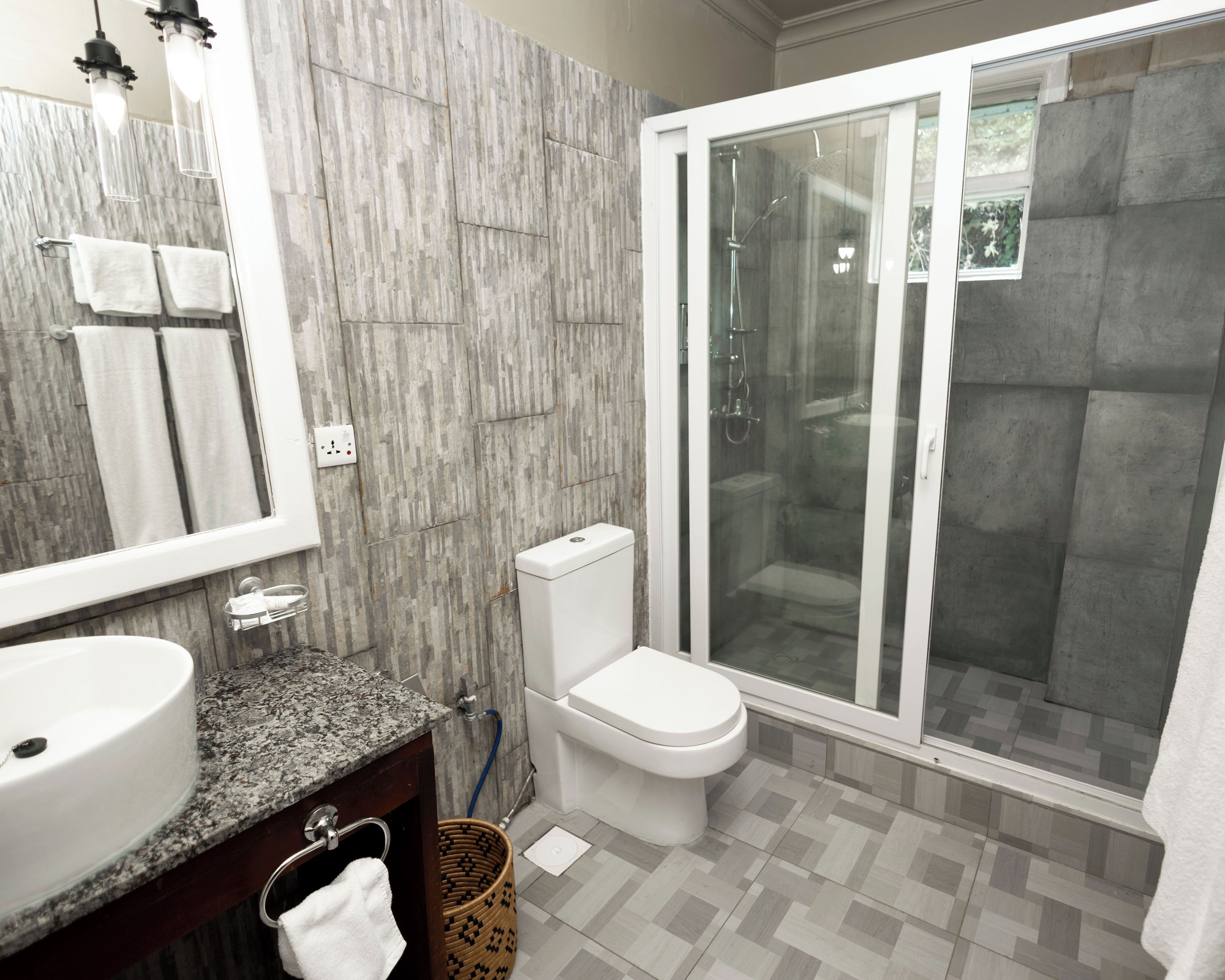 Een badkamer met een wastafel met een granieten blad, een wit toilet en een douche met glazen wanden.