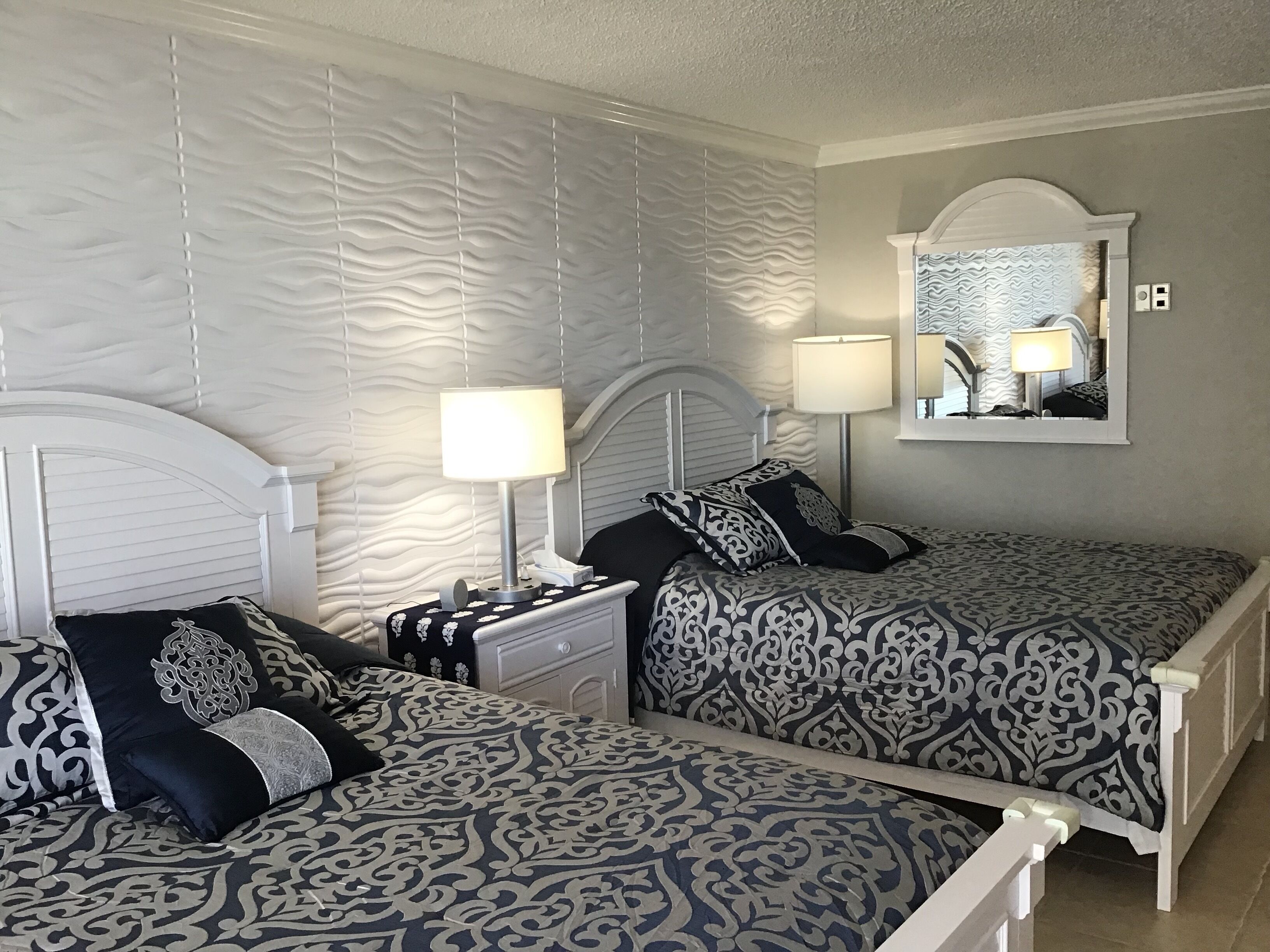 A bedroom with two beds, a nightstand, a mirror, and a lamp.