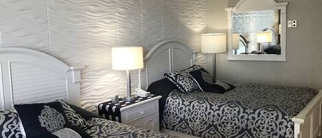 A bedroom with two beds, a nightstand, a mirror, and a lamp.