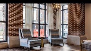 A room with two armchairs, a small table, and a large window with a view of buildings outside.