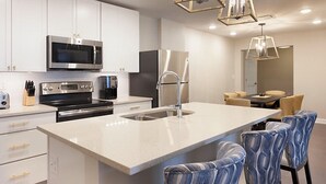 A modern kitchen with stainless steel appliances, a central island with bar stools, and a dining area with a table and chairs.