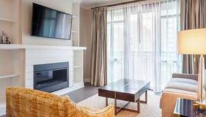 Un salon moderne avec un téléviseur à écran plat fixé au-dessus d’une cheminée, un canapé, une table basse et une lampe.