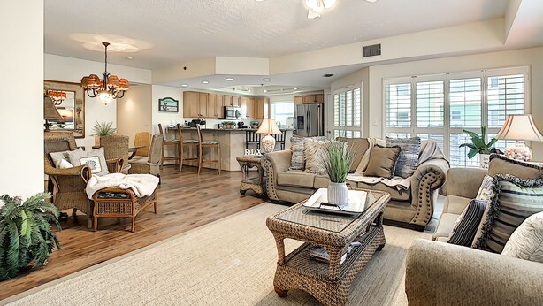 A spacious living area with a high ceiling fan, wicker furniture, and a kitchen in the background. - Oceanwalk 3BR Corner Condo | Private Balcony & 4-Min Walk to Beach (New Smyrna Beach)