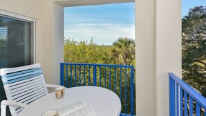 A balcony with a white table, a blue railing, and a view of greenery. - Oceanwalk 3BR Corner Condo | Private Balcony & 4-Min Walk to Beach (New Smyrna Beach)