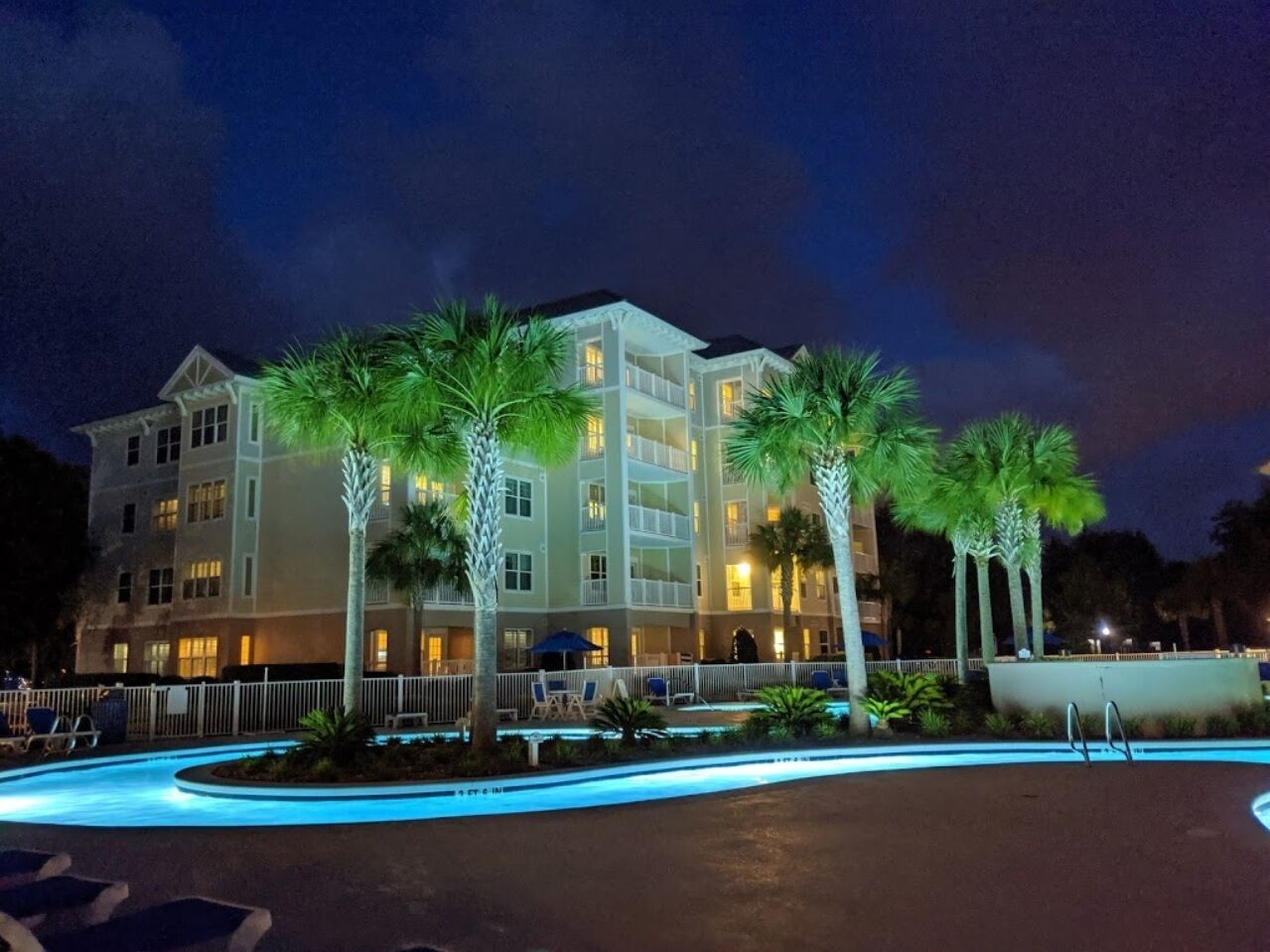 A multi-story hotel with a swimming pool, palm trees, and outdoor seating.