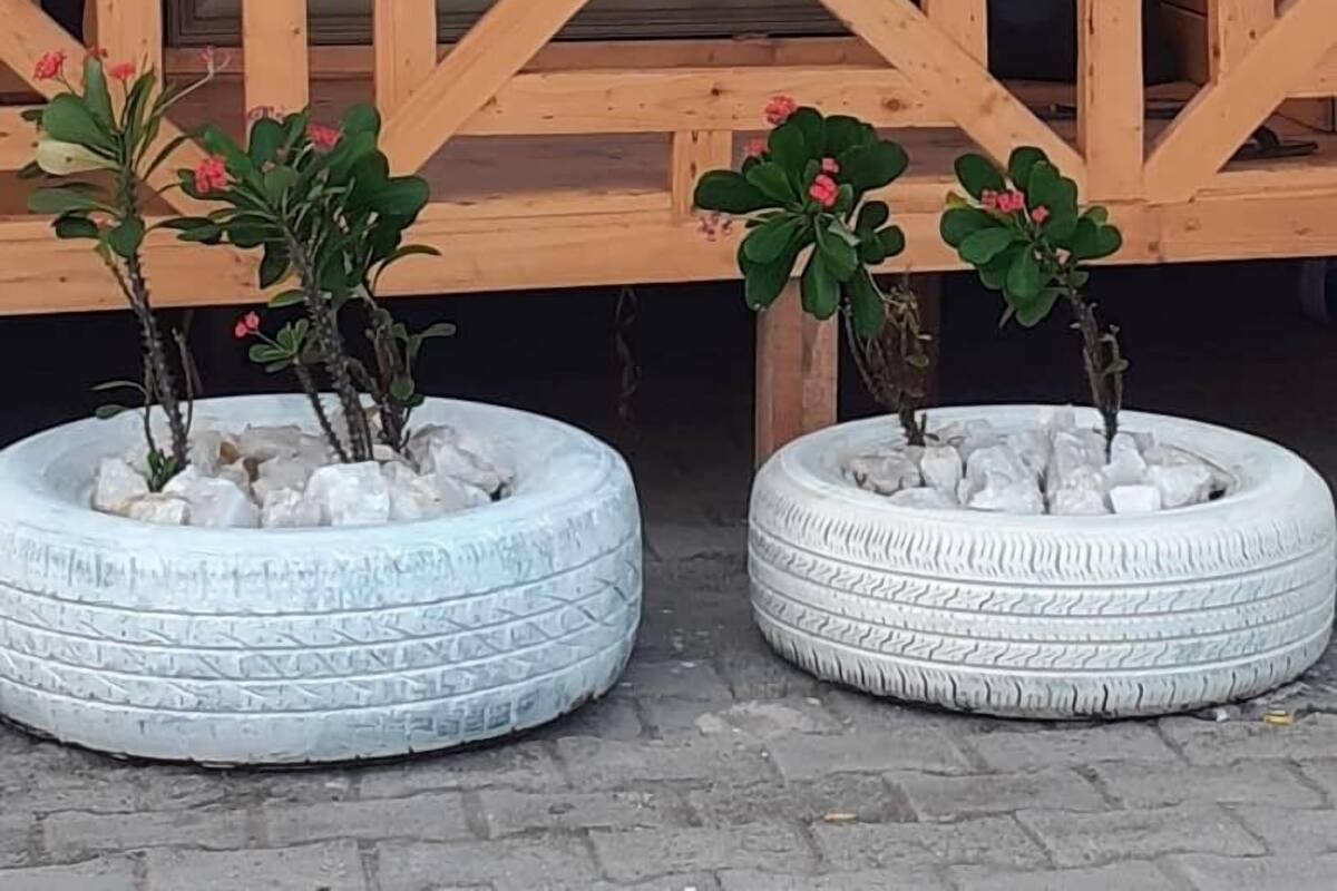 Una estructura de madera con diseño geométrico, posiblemente una terraza o balcón, con dos macetas de neumáticos que contienen plantas pequeñas y rocas.