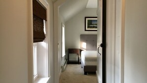 Un couloir étroit, dont le sol est recouvert d’une moquette, mène à une chambre à coucher équipée d’un lit et d’une table de chevet.
