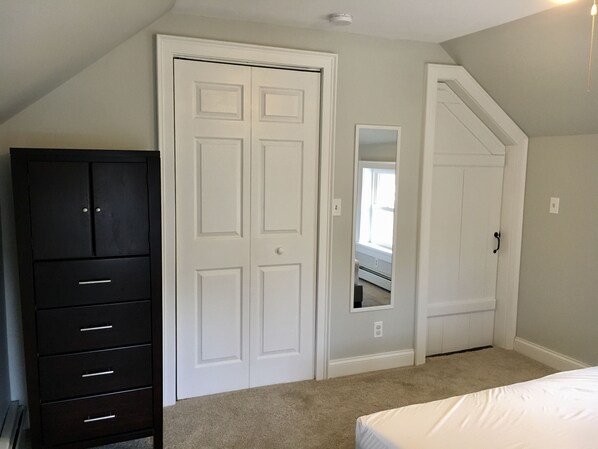 Une chambre avec une commode en bois foncé, une porte blanche et un lit recouvert de linge de lit blanc.