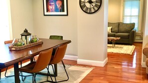 Un coin repas avec une table et des chaises en bois, un tableau encadré au mur et une grande horloge.