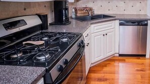 Une cuisine avec des meubles blancs, un lave-vaisselle en acier inoxydable, une cuisinière noire et un four à micro-ondes.