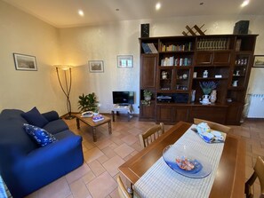 A living room with a blue sofa, a coffee table, a TV, a bookshelf, and a dining area with a table and chairs. - Central and new apartment 15 min. from Colosseum - Metro Re di Roma - Free WiFi (ROMA)