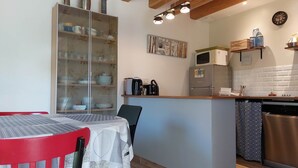 A compact kitchen with a dining area, featuring a refrigerator, microwave, sink, and a cabinet with dishes. - Gite des 3 Provinces (COUFFY)