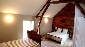 A bedroom with a sloped ceiling, a wooden headboard, a bed with white bedding, and a brick accent wall. - Gite des 3 Provinces (COUFFY)