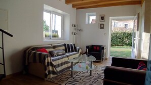 A cozy living room with a sofa, a glass coffee table, and a view of a garden through a window. - Gite des 3 Provinces (COUFFY)